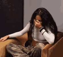 a woman with long hair is sitting in a chair covering her face with her hand .