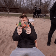 a man in a black jacket is sitting in a chair holding two water guns