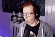 a man wearing headphones and glasses is talking into a microphone in a room .