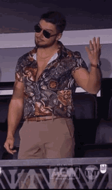 a man wearing sunglasses and a colorful shirt is standing in a stadium watching a game