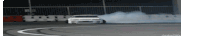 a white car is drifting on a track with smoke coming out of it