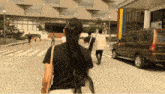 a woman in a black shirt walks down a street with a brown car in the background