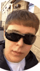 a young man wearing sunglasses and a black jacket looks at the camera