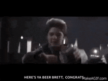 a young boy is holding a glass of beer and says here 's ya beer brett congrats makeagif.com
