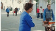 a woman in a blue sweater smiles while walking down a street