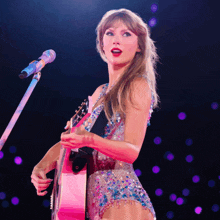 a woman singing into a microphone while holding a pink guitar