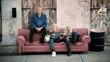 three men sit on a pink couch in front of a building with a no parking sign on it