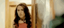 a woman in a red dress is standing in front of a door looking at the camera .