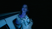 a woman with purple paint on her face is sitting in a dark room