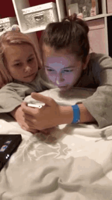 two young girls are laying on a bed looking at a phone .