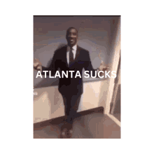 a man in a suit and tie stands in a hallway with atlanta sucks written on the bottom