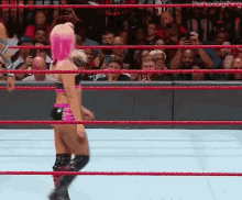 a woman with pink hair is standing in a wrestling ring with a crowd watching .