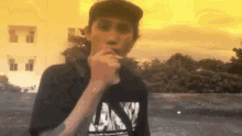 a young man is smoking a cigarette while wearing a black shirt with the letter n on it .