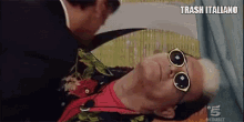 a man wearing sunglasses is laying on a bed next to a man in a suit and tie .