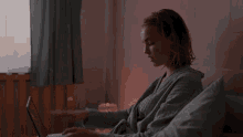 a woman in a bathrobe is sitting on a bed looking at her watch .