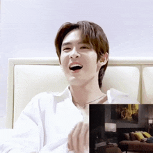 a man in a white shirt is sitting on a bed and laughing
