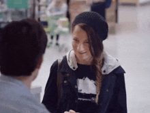 a woman wearing a black beanie and a black jacket is talking to a man
