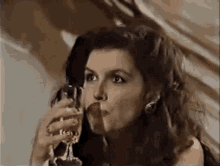 a woman is holding a glass of wine in her hand and drinking it .
