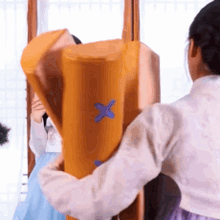 a woman in a white shirt is holding a yellow object with a blue x on it .