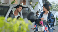 a man and a woman are talking in front of a car and a motorcycle with a license plate that says ncj