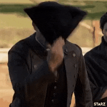 a man is covering his face with a black hat while standing next to another man .