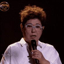 a woman wearing glasses and a white shirt holds a microphone in her hand