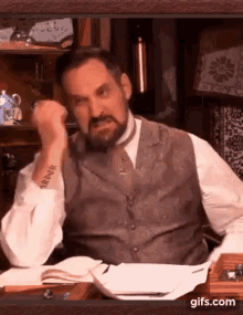 a man with a beard and a tattoo on his arm is sitting at a table with a book and dice .