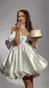 a woman in a white dress is holding a cake and licking her lips .