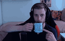 a man wearing headphones is drinking from a mug that says " i drink a lot " on it