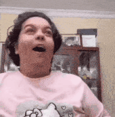 a woman in a pink hello kitty shirt is making a funny face with her mouth open .