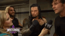 a group of wrestlers are talking in front of a wrestlemania advertisement