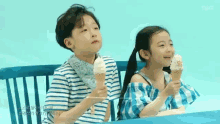 a boy and a girl are sitting on a bench eating ice cream cones .