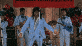 a man in a blue suit is singing into a microphone in front of a band