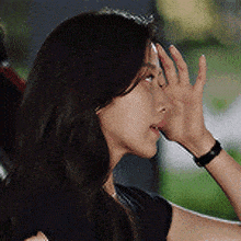 a woman is covering her face with her hand while wearing a black shirt .