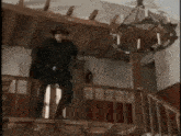 a man in a mask is standing on a balcony in a room with a chandelier .