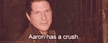 a man is standing in front of a fence and saying `` aaron has a crush '' .