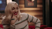 a blonde woman is sitting on a red couch wearing a striped sweater and red lipstick .