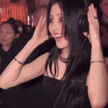 a woman wearing headphones is smiling with her hands on her head