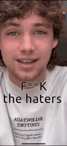 a man with curly hair and a beard is wearing a white shirt that says f ** k the haters .