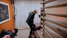 a man in a black jacket is standing next to a wooden fence in a bedroom .