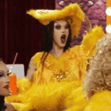 a drag queen wearing a yellow feathered hat and a yellow dress