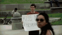 a man is holding a sign that says kiss me despera