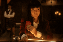 a woman in a red jacket holds a deck of cards