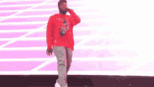 a man in a red shirt is singing into a microphone while walking on a stage