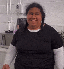 a woman in a black shirt is smiling in front of a white wall