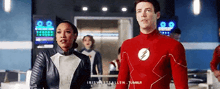 a man and a woman are standing next to each other in a room in a flash suit .