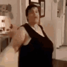 a woman in a black dress is standing in a kitchen and looking at the camera .