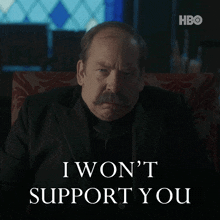 a man with a mustache is sitting in a chair and says i won t support you