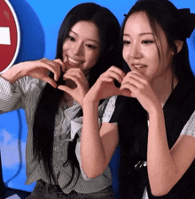 two women make a heart shape with their hands in front of a no entry sign