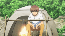 a boy sits in front of a tent with a fire